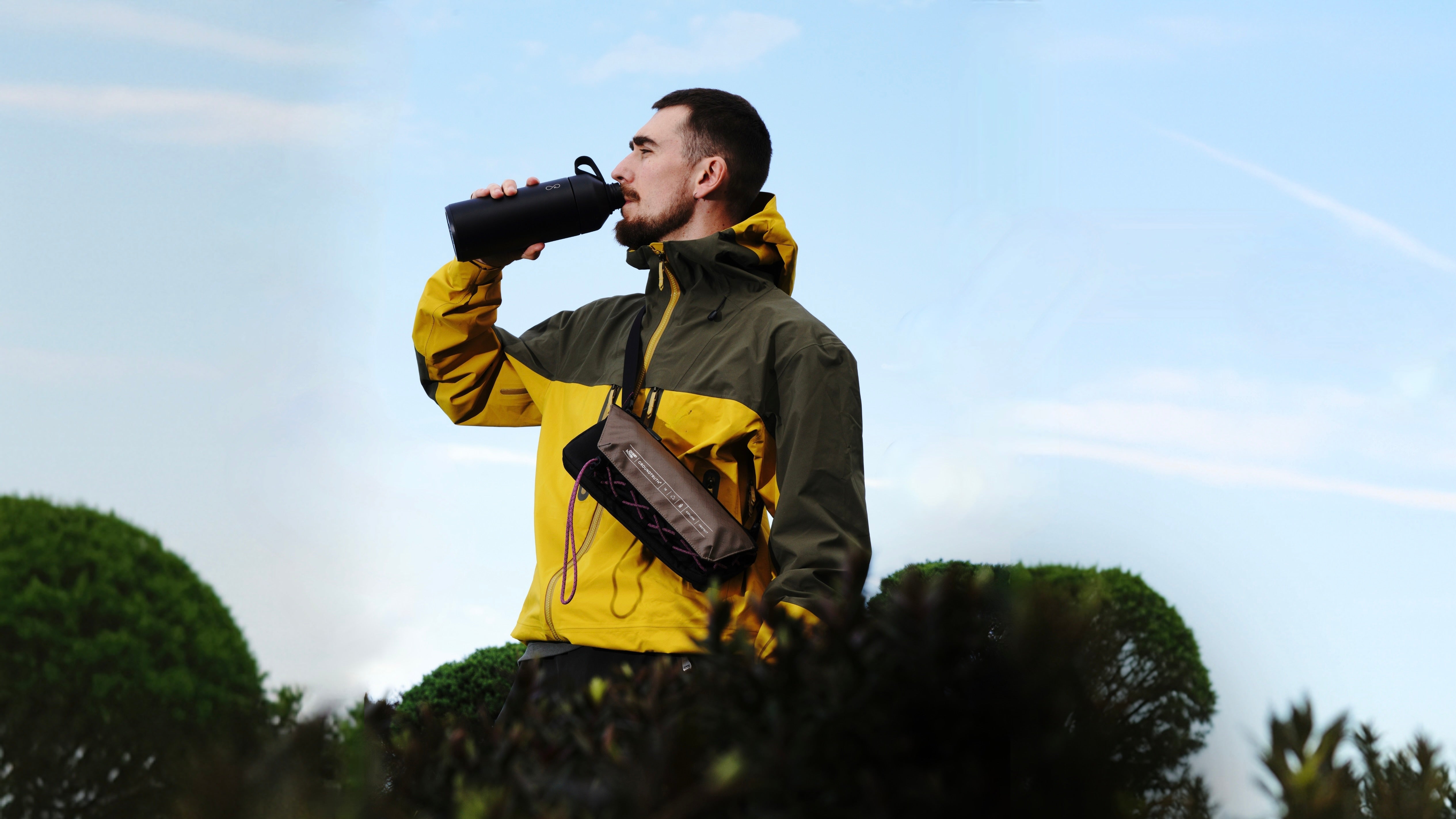Man in a yellow jacket drinking from a Ocean bottle with The new GROUNDTRUTH Bottle bag 